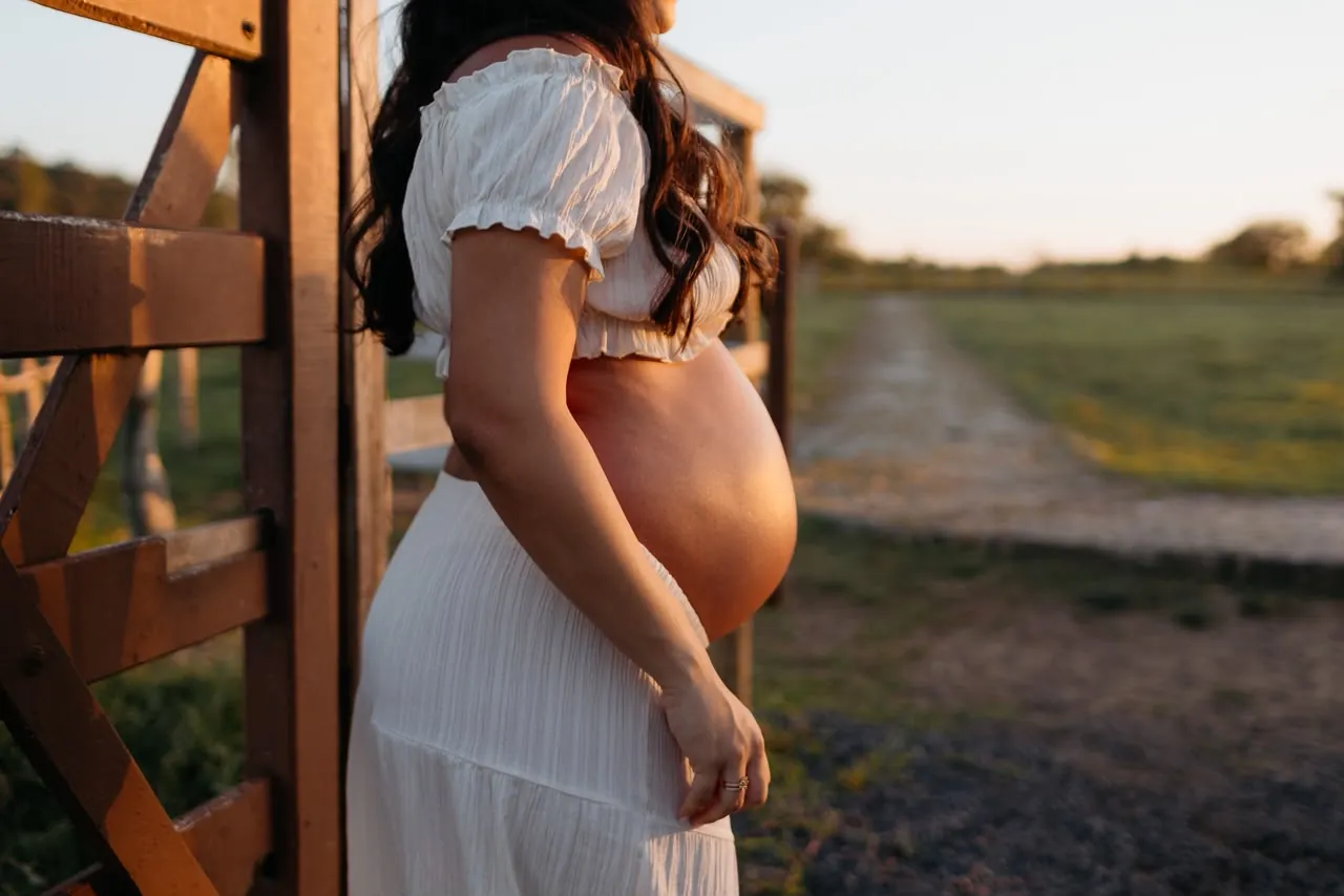 Barriga de gestante na porteira, ao entardecer