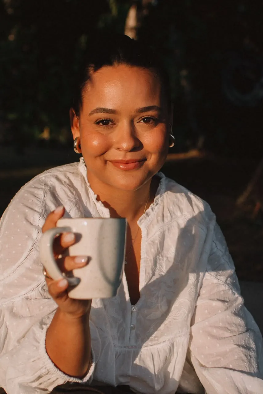 Júlia com uma caneca, no jardim, na luz do fim de tarde